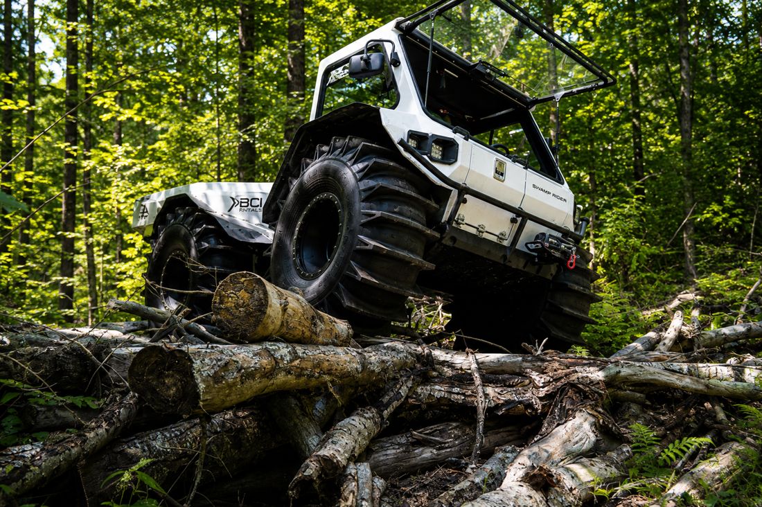 Swamp Rider climbing over downed logs on a forested right-of-way
